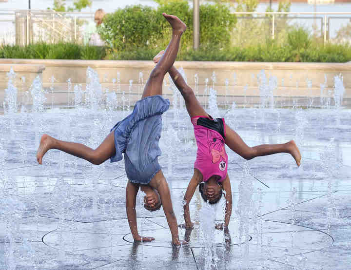 Alisha Brake and her sister Isabella Brake do cartwheels at the Promenade Park splash pad in Toledo.  (Jeremy Wadsworth / The Blade)